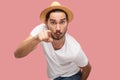 Portrait of shocked bearded young man in white shirt with hat standing, looking and pointing at camera with surprised face Royalty Free Stock Photo