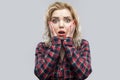 Portrait of shocked beautiful blonde young woman in casual red checkered shirt standing, touching her face and looking at camera Royalty Free Stock Photo