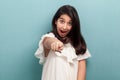 Portrait of shocked beautiful brunette young girl with black long straight hair in white dress standing looking and pointing at Royalty Free Stock Photo