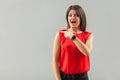 Portrait of shocked beautiful brunette young woman in red shirt standing, looking, amazed surprised face and pointing at empty Royalty Free Stock Photo