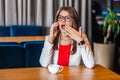 Portrait of shocked beautiful stylish brunette young woman in glasses sitting listeting amazed news on her mobile smart phone and Royalty Free Stock Photo