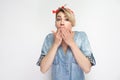 Portrait of shocked beautiful young woman in casual blue denim shirt, makeup and red headband standing and covering her mouth and Royalty Free Stock Photo