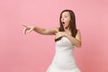 Portrait of shocked bride woman with opened mouth in white wedding dress standing pointing index fingers aside