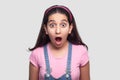 Portrait of shocked brunette young girl in casual style, pink t-shirt and blue overalls standing with big eyes and open mouth Royalty Free Stock Photo