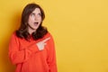 Portrait of shocked caucasian female with pleasant appearance indicates aside at blank yellow wall  has surprised and astonished Royalty Free Stock Photo