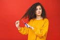 Portrait of shocked curly girl cutting her hair with scissors, isolated on red background Royalty Free Stock Photo