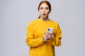 Portrait of shocked young woman wearing yellow sweater holding mobile phone and looking at camera Royalty Free Stock Photo