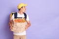 Portrait of shocked delivery man wearing cap holding pizza boxes in hands, looking away with astonishment at copy space for