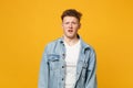 Portrait of shocked disgusted young man in denim casual clothes standing and looking camera isolated on yellow orange