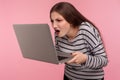 Portrait of shocked displeased angry girl in striped sweatshirt looking closer at laptop screen, unpleasantly surprised