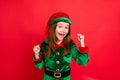 Portrait of shocked elf kid in green hat cap with long red head hairstyle raising her fists celbrate newyear party Royalty Free Stock Photo