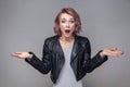 Portrait of shocked girl with short hairstyle, makeup in black leather jacket standing raised arms and looking at camera with big Royalty Free Stock Photo