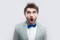 Portrait of shocked handsome bearded man in casual grey suit and blue bow tie standing with big eyes and open mouth and looking at Royalty Free Stock Photo