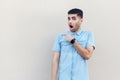 Portrait of shocked handsome young bearded man in blue shirt standing, looking at camera with surprised face and pointing at Royalty Free Stock Photo