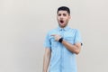 Portrait of shocked handsome young bearded man in blue shirt standing pointing at his right side and looking at camera with Royalty Free Stock Photo
