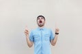 Portrait of shocked handsome young bearded man in blue shirt standing pointing at his up copyspace and looking with surprised face Royalty Free Stock Photo