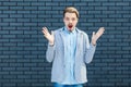 Portrait of shocked handsome young blonde man in casual style standing with raised arms and looking at camera with unbelievable