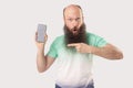 Portrait of shocked middle aged bald bearded man standing with mobile smart phone pointing at empty screen and looking with Royalty Free Stock Photo