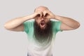 Portrait of shocked middle aged bald man with long beard in light green t-shirt standing with binocular hands on eyes and looking Royalty Free Stock Photo