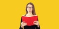 Portrait of shocked student girl in eyeglasses looking in the opened book on yellow background Royalty Free Stock Photo