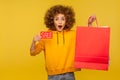 Portrait of shocked surprised curly-haired hipster girl in hoodie holding shopping bags with blank area Royalty Free Stock Photo