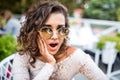 Portrait of shocked and surprised latin womanin sunglasses in cafe with amazed and afraid expression