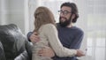 Portrait of shocked unhappy Caucasian man in eyeglasses embracing his wife. Woman showing affirmative pregnancy test and