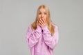 Portrait of shocked unhappy young blonde woman covering mouth with hands, hear bad news, problem trouble, wears violet hoody, Royalty Free Stock Photo