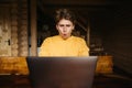 Portrait of shocked young man in casual clothes using laptop in wooden country house. Work on the Internet Royalty Free Stock Photo