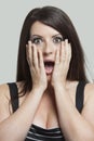 Portrait of shocked young woman with hands on face against gray background