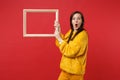 Portrait of shocked young woman in yellow fur sweater keeping mouth wide open, hold picture frame isolated on red