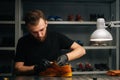 Portrait of shoemaker wearing black latex gloves applying paint on light brown leather shoes and rubbing with fingers.