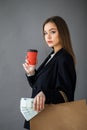 Portrait of shopaholic beautiful woman wearing suit holding money cash, cup of coffe and paper shopping bags isolated over grey