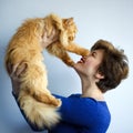 Portrait of short haired beautiful 30 years old woman in blue dress playing with ginger red furry persian cat. Domestic animal, Royalty Free Stock Photo