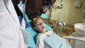 African male dentist checking the teeth of little male patient.