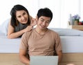Portrait shot of Asian lover couple relaxes at home on the weekends. The wife lies on the bed behind her husband that sits on the Royalty Free Stock Photo