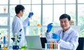 Portrait shot of Asian professional mature male scientist in white lab coat and rubber gloves sitting look at camera smiling