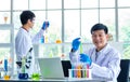 Portrait shot of Asian professional mature male scientist in white lab coat and rubber gloves sitting look at camera smiling