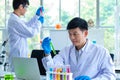 Portrait shot of Asian professional mature male scientist in white lab coat and rubber gloves sitting look at camera smiling