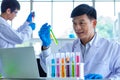 Portrait shot of Asian professional mature male scientist in white lab coat and rubber gloves sitting look at camera smiling