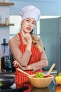 Portrait shot of Asian young beautiful female chef housewife wears white tall cook hat and apron standing smiling posing thinking Royalty Free Stock Photo