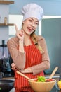 Portrait shot of Asian young beautiful female chef housewife wears white tall cook hat and apron standing smiling posing thinking Royalty Free Stock Photo