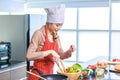 Portrait shot of Asian young female chef housewife wears white tall cook hat and apron standing smiling holding wooden spoon fork Royalty Free Stock Photo