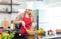 Portrait shot of Asian young female chef housewife wears white tall cook hat and apron standing smiling holding wooden spoon fork Royalty Free Stock Photo