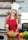 Portrait shot of Asian young female chef housewife wears white tall cook hat and apron standing smiling holding wooden spoon fork Royalty Free Stock Photo