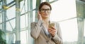 Portrait shot of the Caucasian attractive businesswoman in glasses putting on headphones, taping on the smartphone and