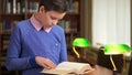 Portrait shot of the cute schoolboy and standing near the bookshelf in the library and reading a book. Royalty Free Stock Photo