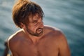 Portrait shot of handsome shirtless muscular man in front of blurred water background. Holiday, lifestyle, lesiure concept