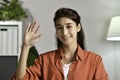 Portrait shot of happy friendly and confident Asian businesswoman sitting on a desk at home, looking and talking at camera and wav