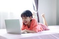 Portrait shot little Asian girl using a laptop computer to learn from home and laying on the bed with happiness, self-quarantine